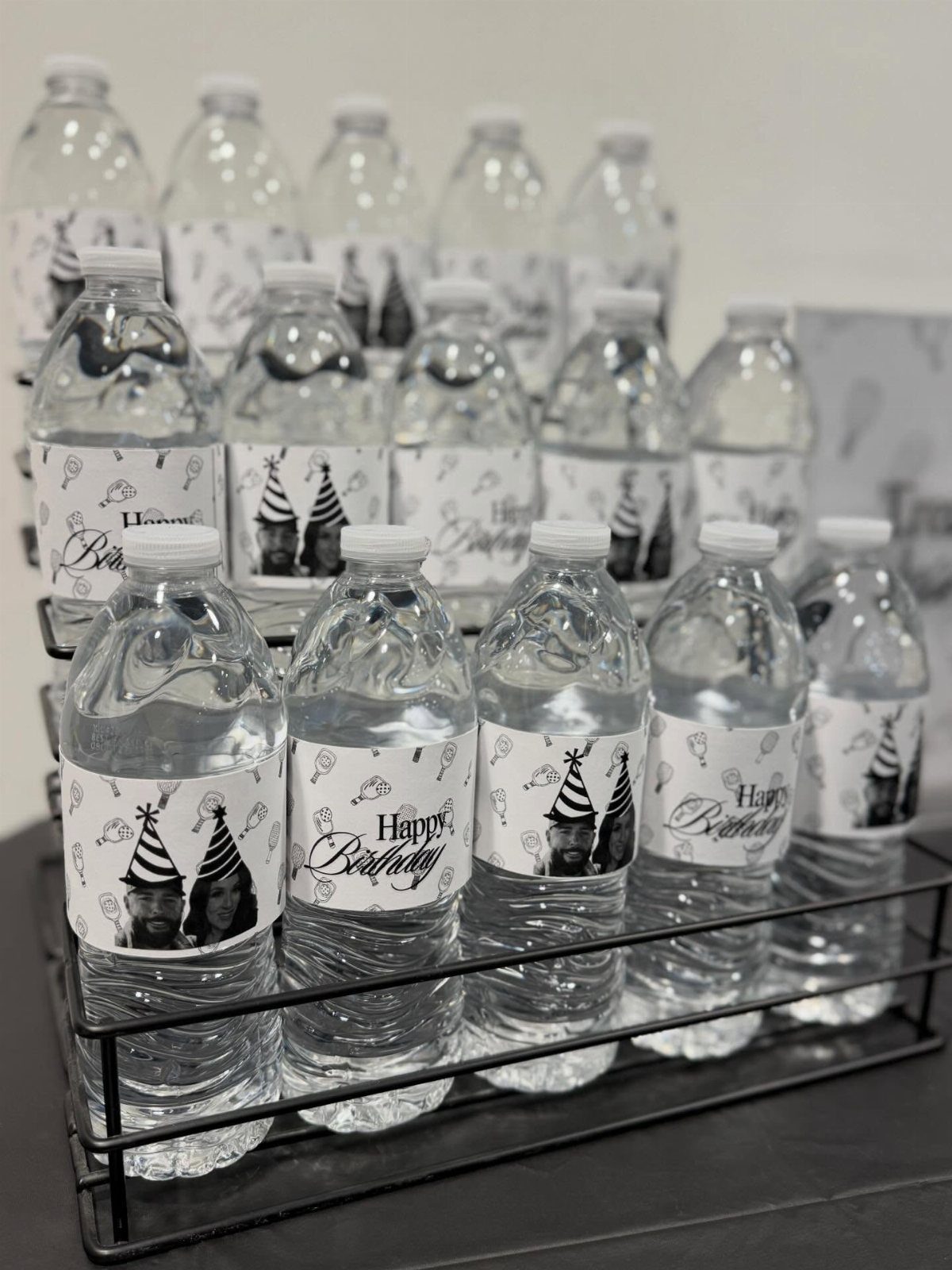 Water bottles in a black rack with custom Happy Birthday photo labels.