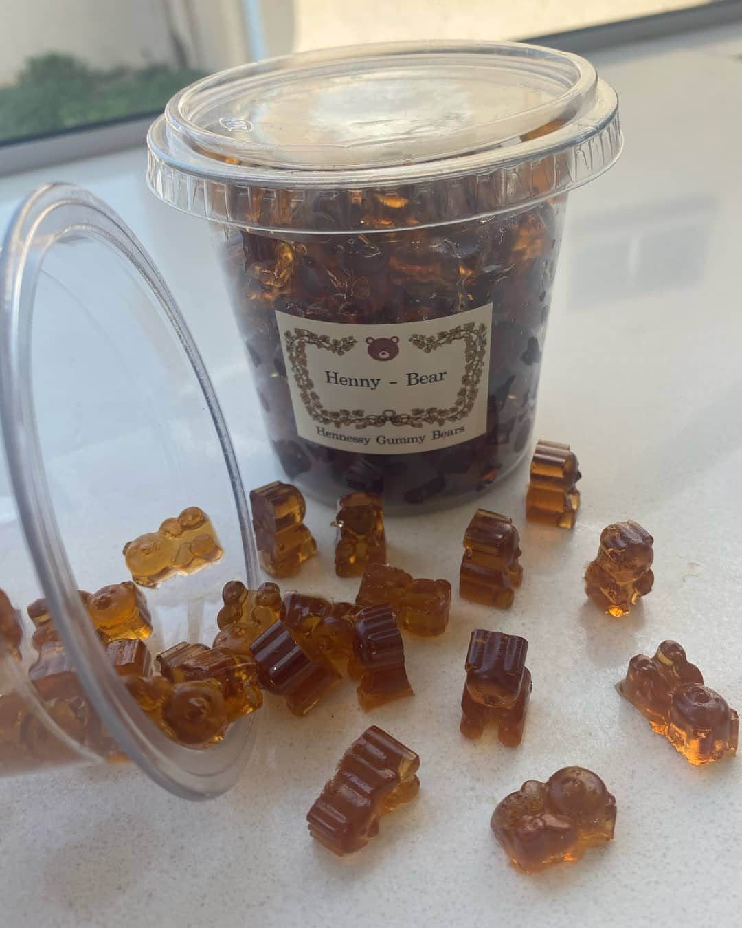 Amber gummy bears in a plastic container and scattered on a white surface.