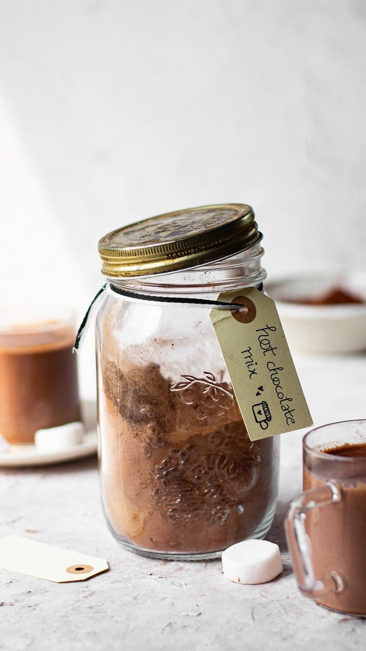 Glass jar of hot chocolate mix with a handwritten tag and cocoa mugs.