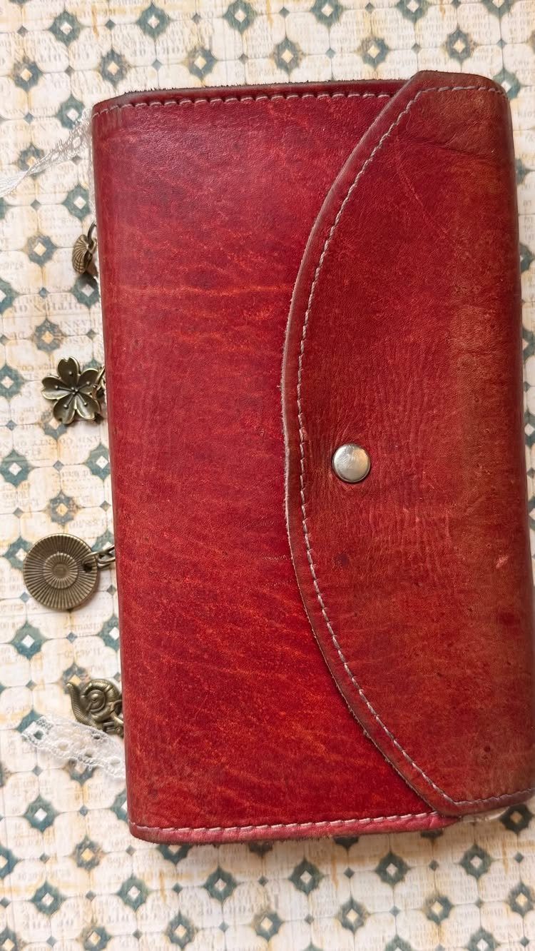 Red leather journal with a snap closure and metal charms on patterned fabric.