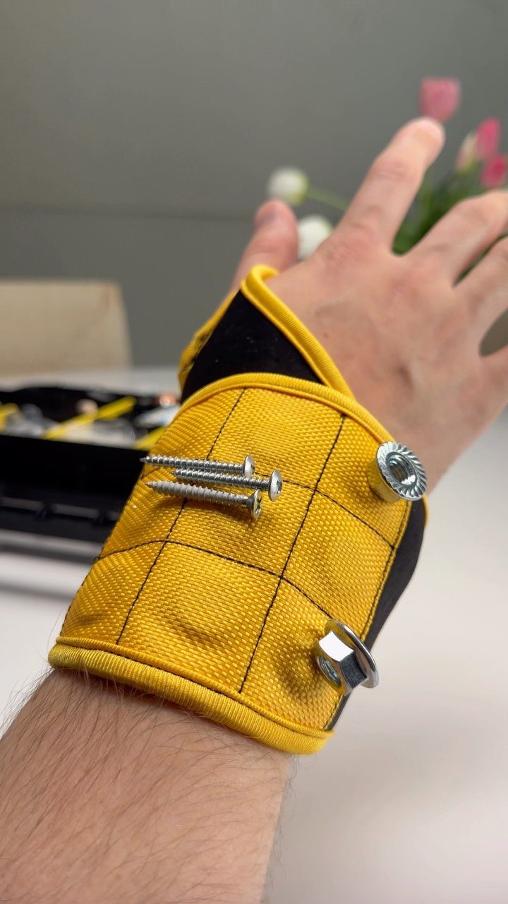 Yellow magnetic wristband on a person's arm holding silver screws and a nut.