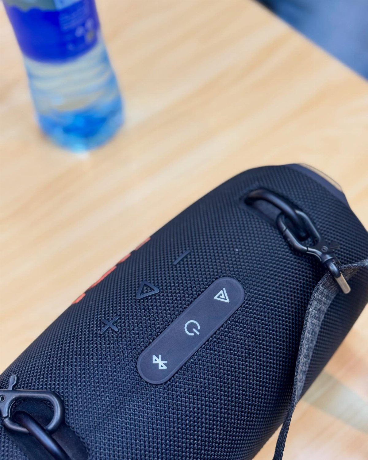 Black portable Bluetooth speaker with a carry strap on a wooden table