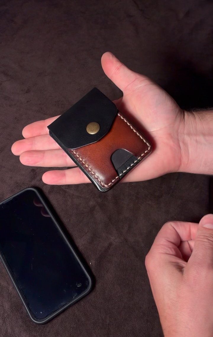 Slim leather wallet with a snap button held in a person's hand.