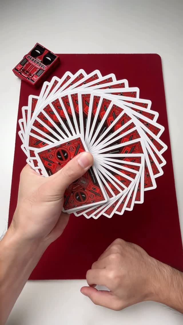 Hands fanning a deck of red and black Deadpool themed playing cards.