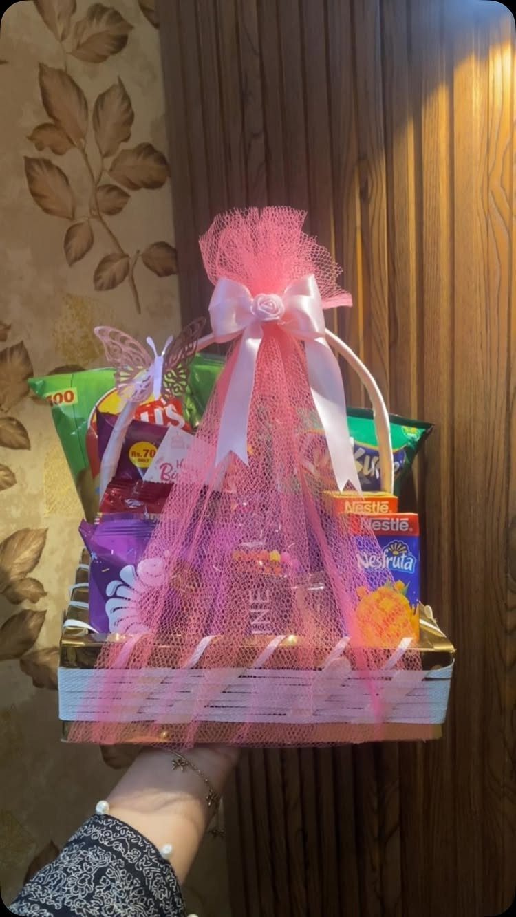 Gift basket filled with snacks and chocolates wrapped in pink tulle and ribbon.