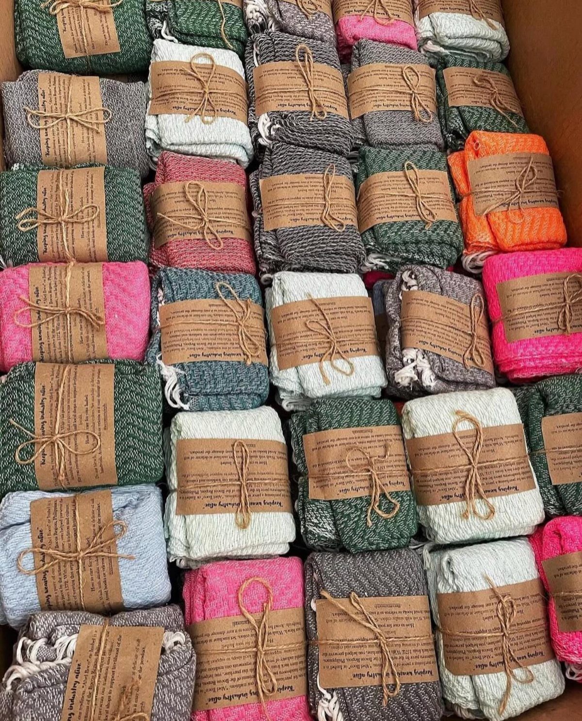 Folded colorful textured dish towels wrapped with brown paper bands and twine.