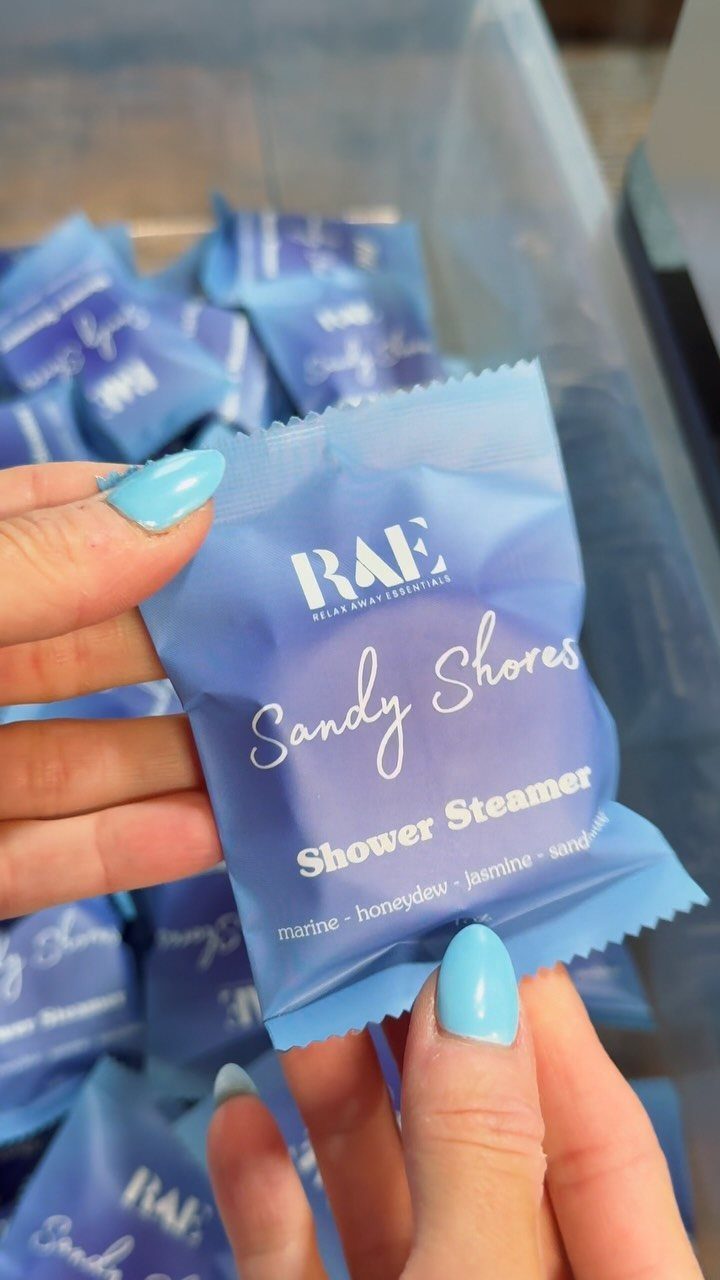 Hand holding a blue Sandy Shores shower steamer packet over a bin of packets
