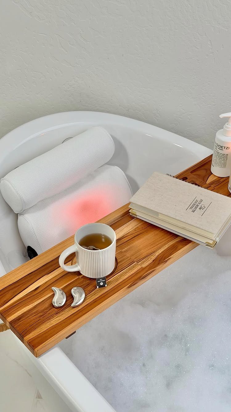 White bath pillow and wooden caddy with tea and notebook in bubbly bathtub