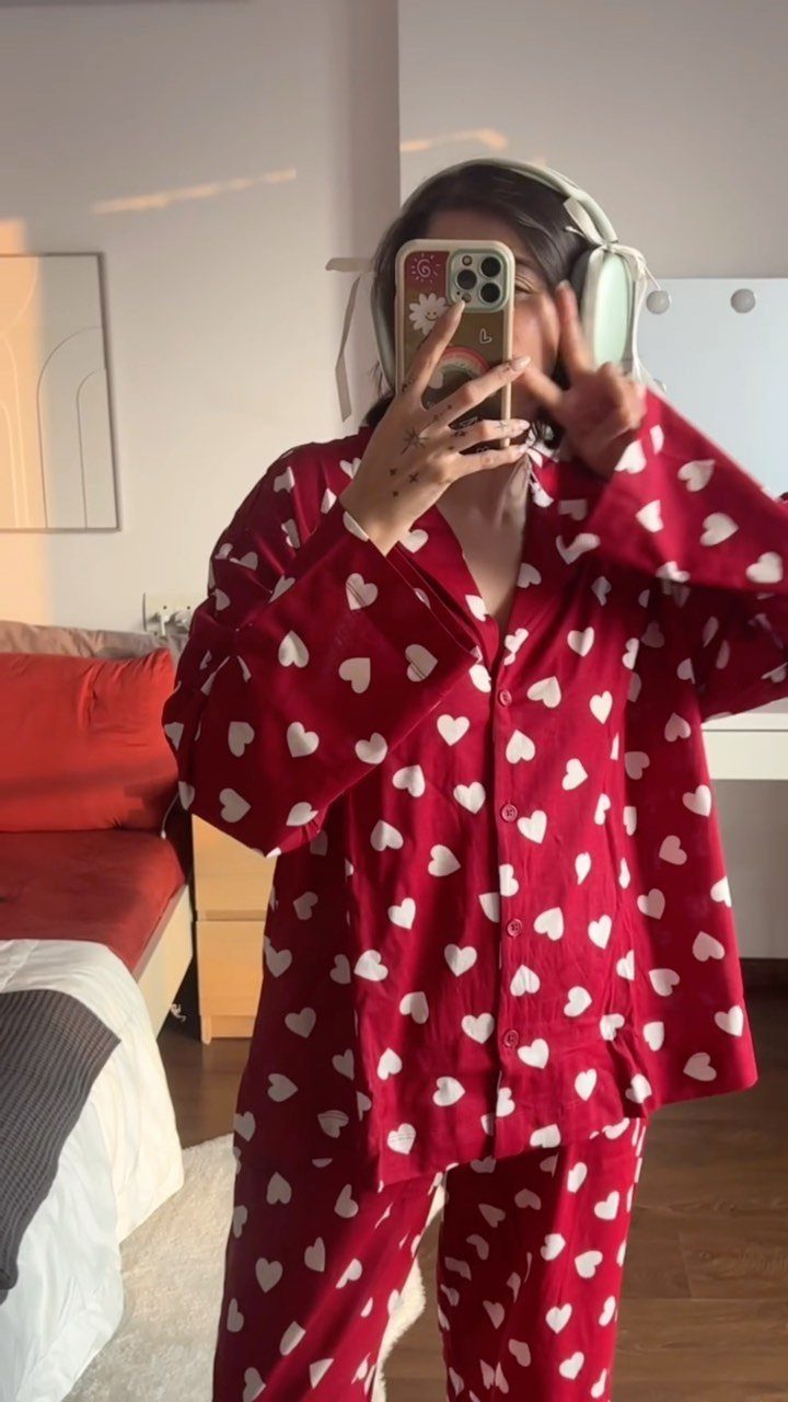 Woman wearing red pajamas with white hearts taking a mirror selfie in a bedroom.