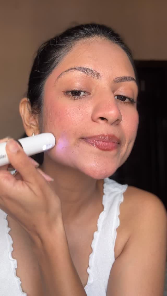 Woman using a white electronic skincare device on her cheek for facial care.