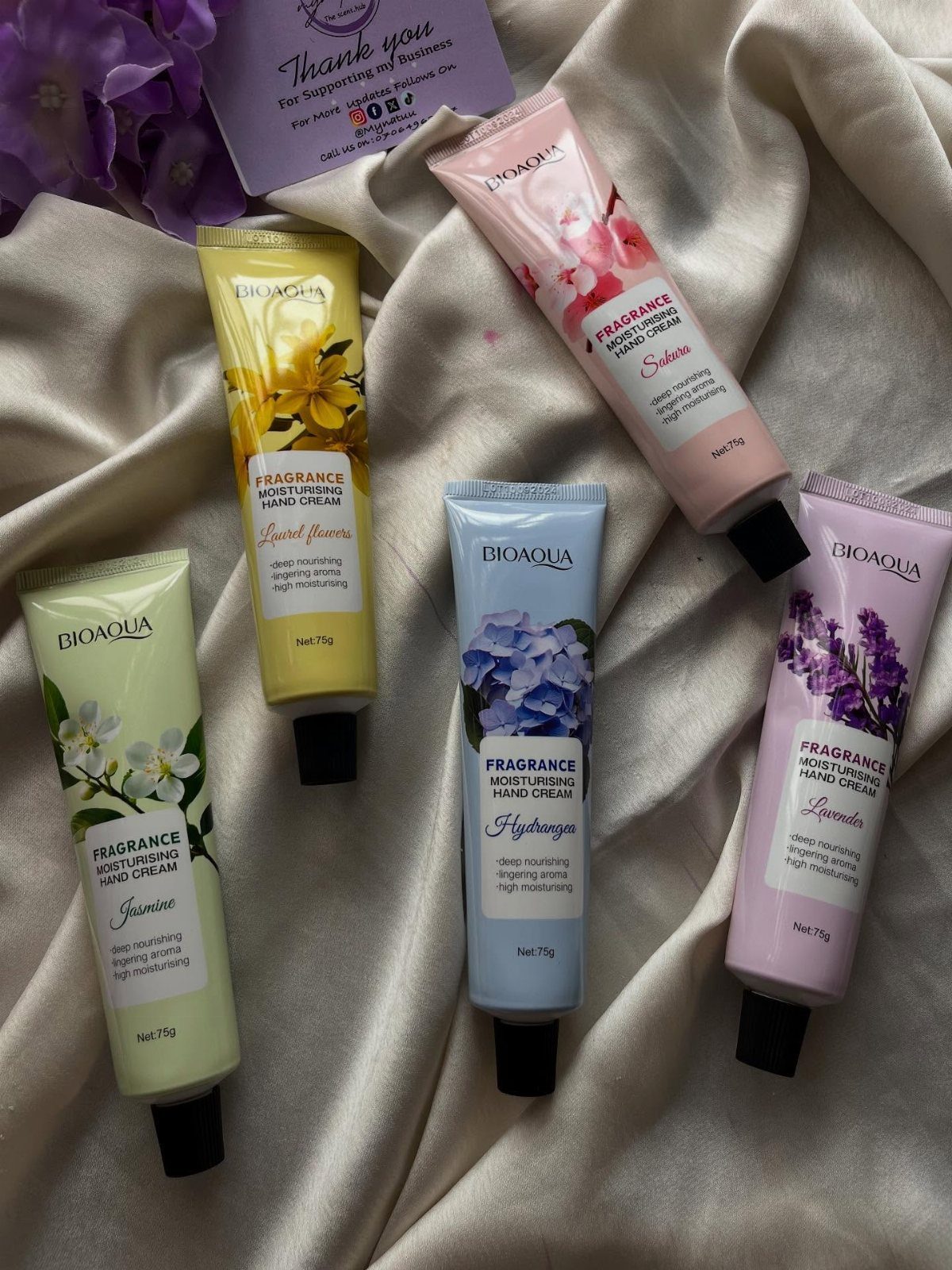 Five colorful tubes of moisturizing hand cream arranged on cream fabric with flowers.