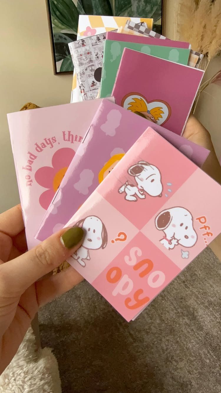 Hand holding a collection of colorful mini notebooks with Snoopy illustrations.