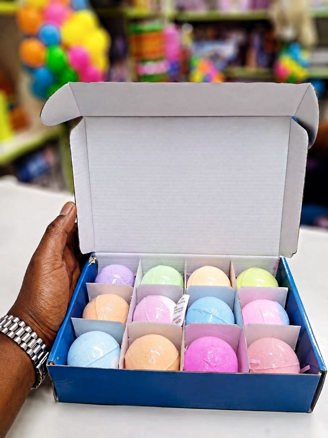 Colorful pastel bath bombs arranged in a blue gift box held by a hand.
