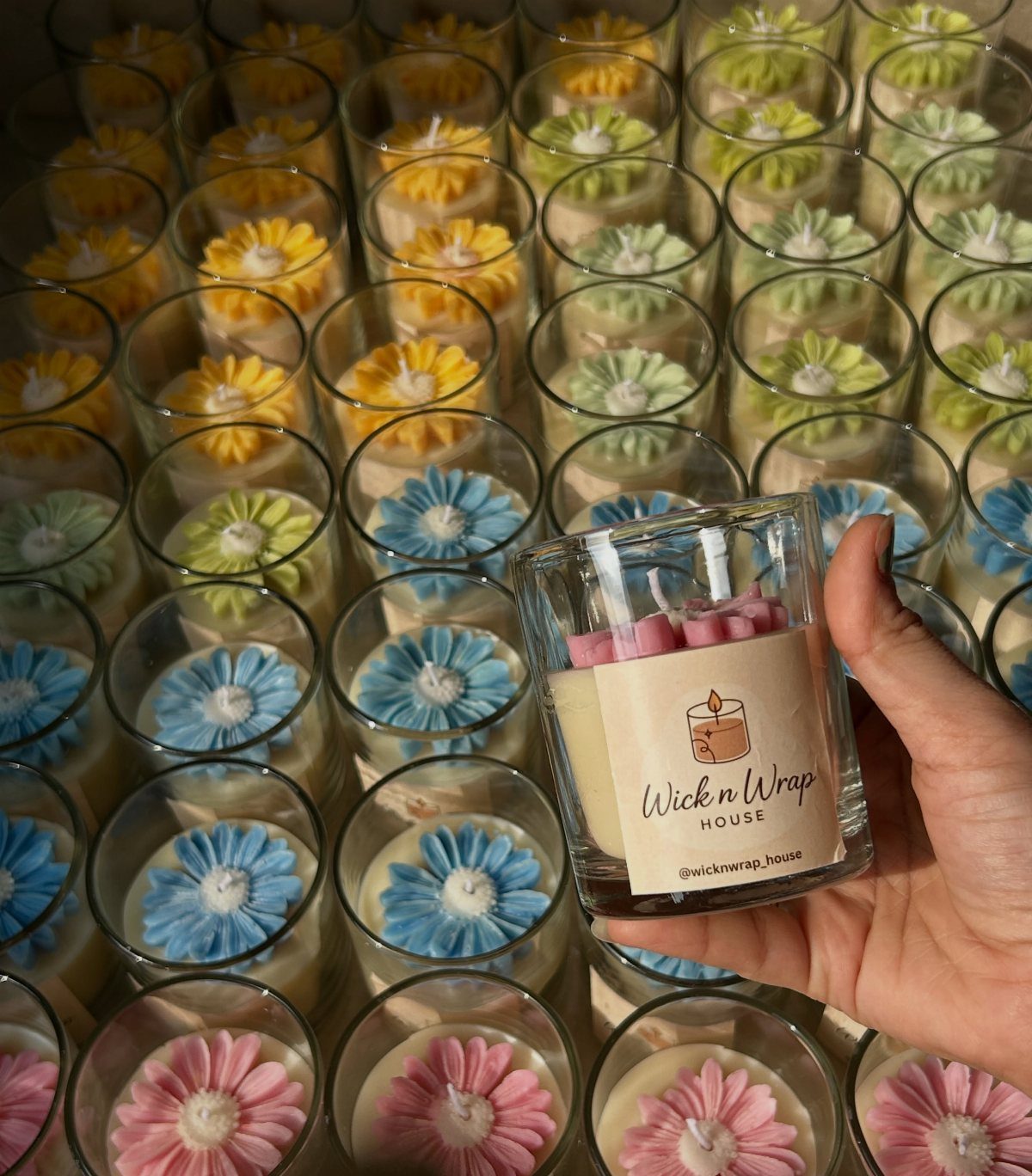 Hand holding a decorative flower candle surrounded by many colorful floral candles.
