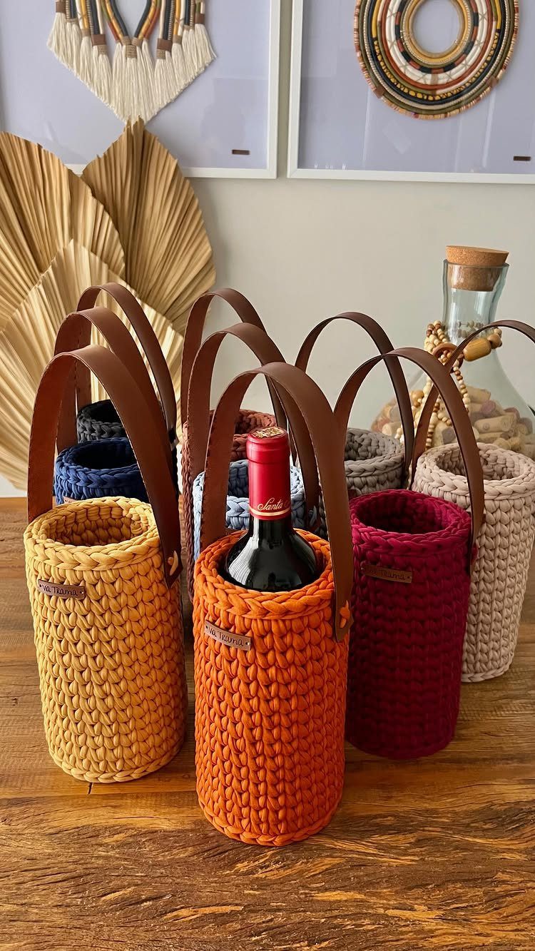 Crocheted wine bottle holders in various colors with leather handles on wooden table