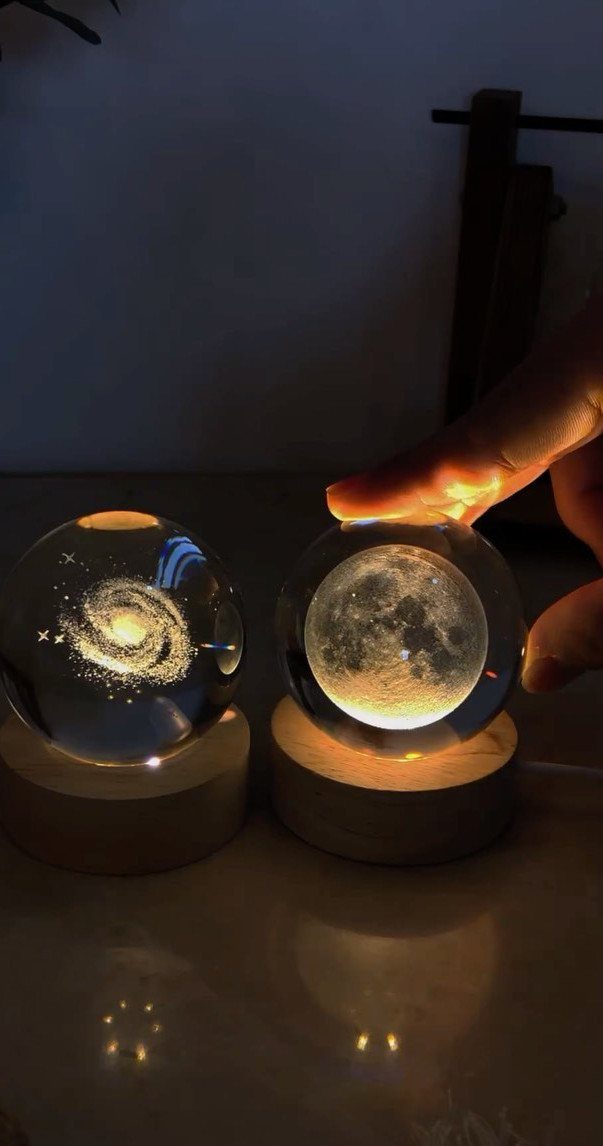 Two illuminated crystal spheres showing a galaxy and the moon on wooden bases.