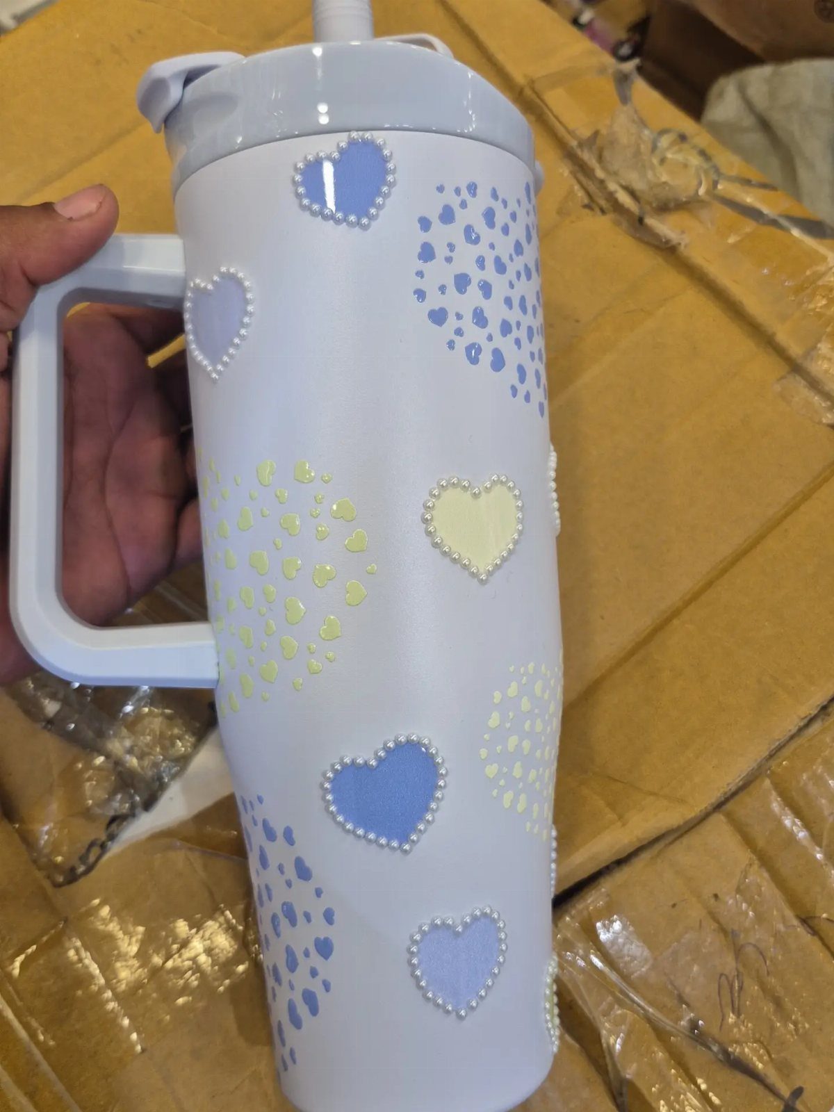 Light blue insulated tumbler decorated with small colorful raised heart patterns.