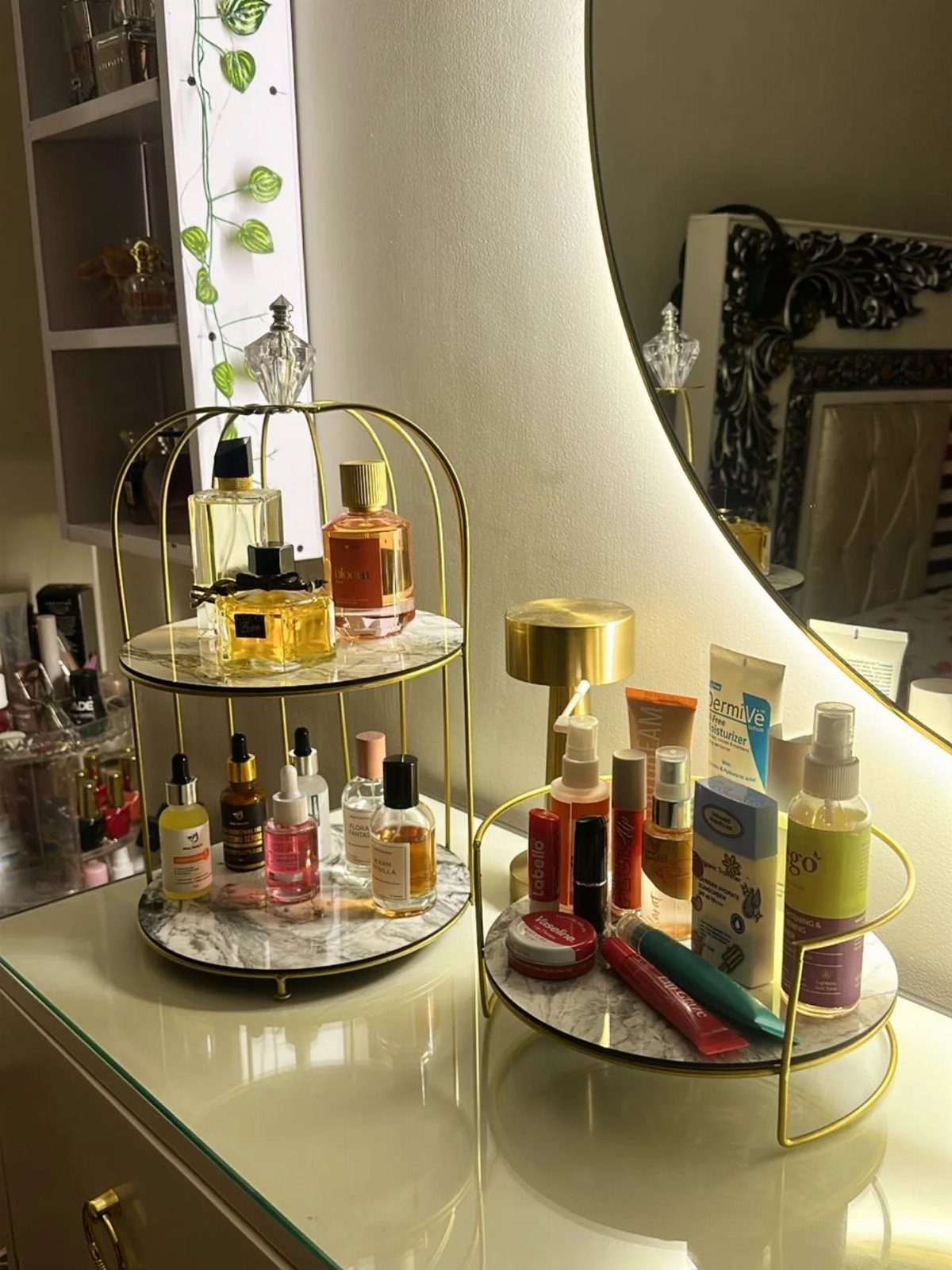 Gold tiered cosmetic display case holding perfumes and skincare on a white vanity.