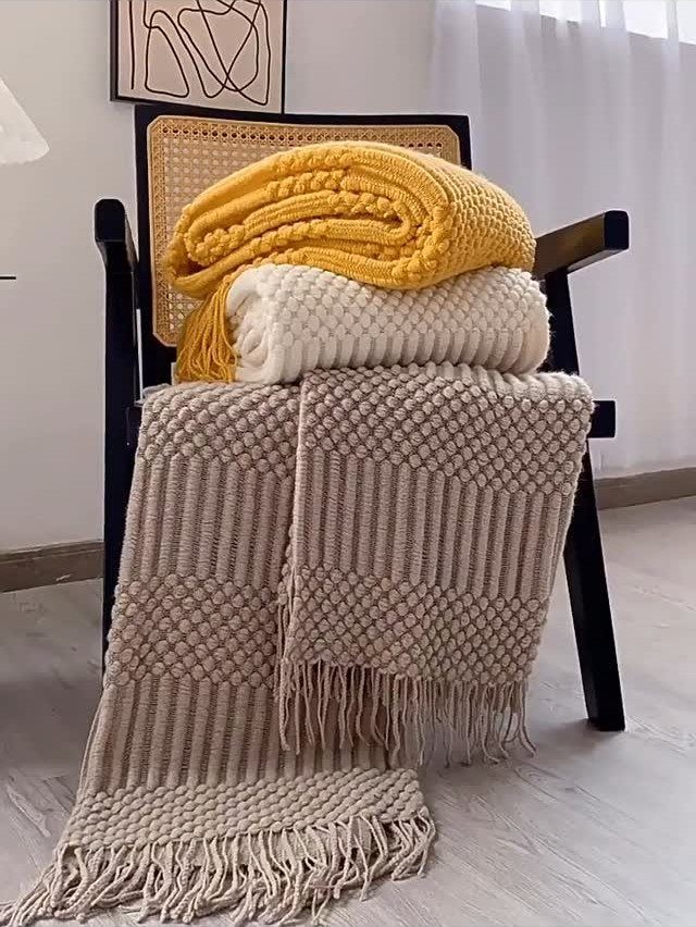 Three knitted blankets in yellow, white, and beige stacked on a black chair.