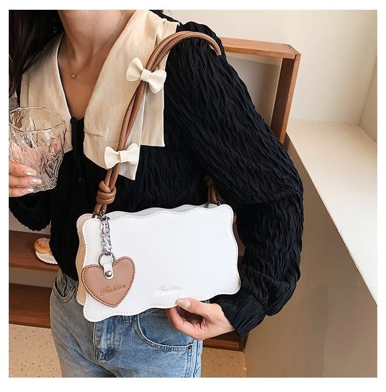 Small white scalloped handbag with brown straps and heart charm held by woman