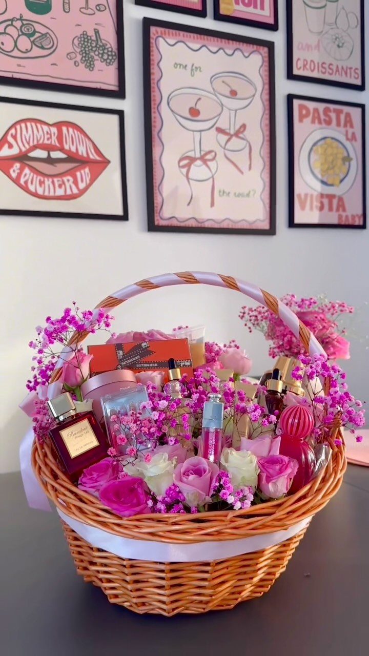 Wicker gift basket filled with pink roses, perfumes, and cosmetics against art prints.