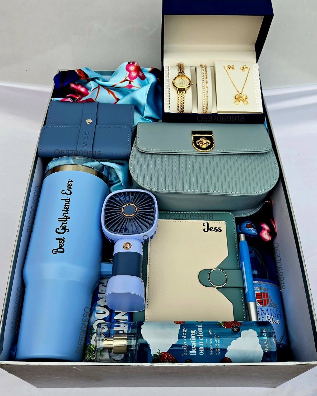 Gift box with personalized tumbler and notebook, blue handbag, and gold jewelry.