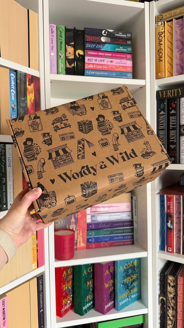 Brown Wordy & Wild subscription box held in front of white bookshelves with books