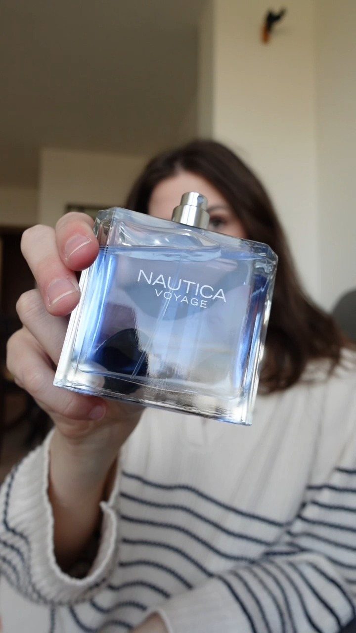 Nautica Voyage cologne bottle held up by a person in a striped shirt.