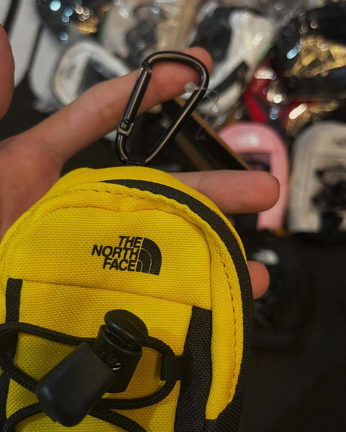 Yellow The North Face small pouch with black carabiner held in a hand