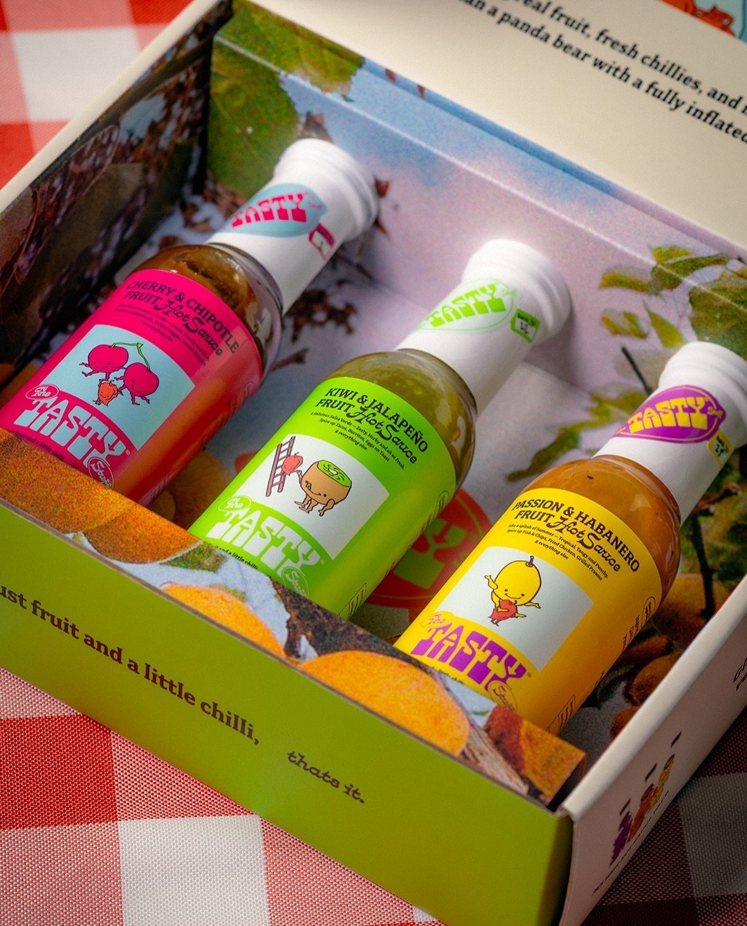 Three colorful bottles of fruit hot sauce inside a branded gift box.