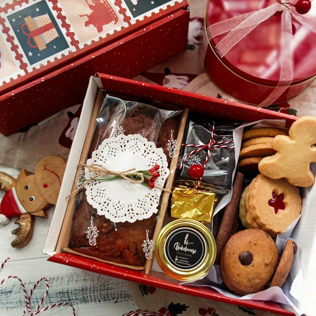 Red gift box containing fruitcake, jam, and assorted cookies for holiday gifting.