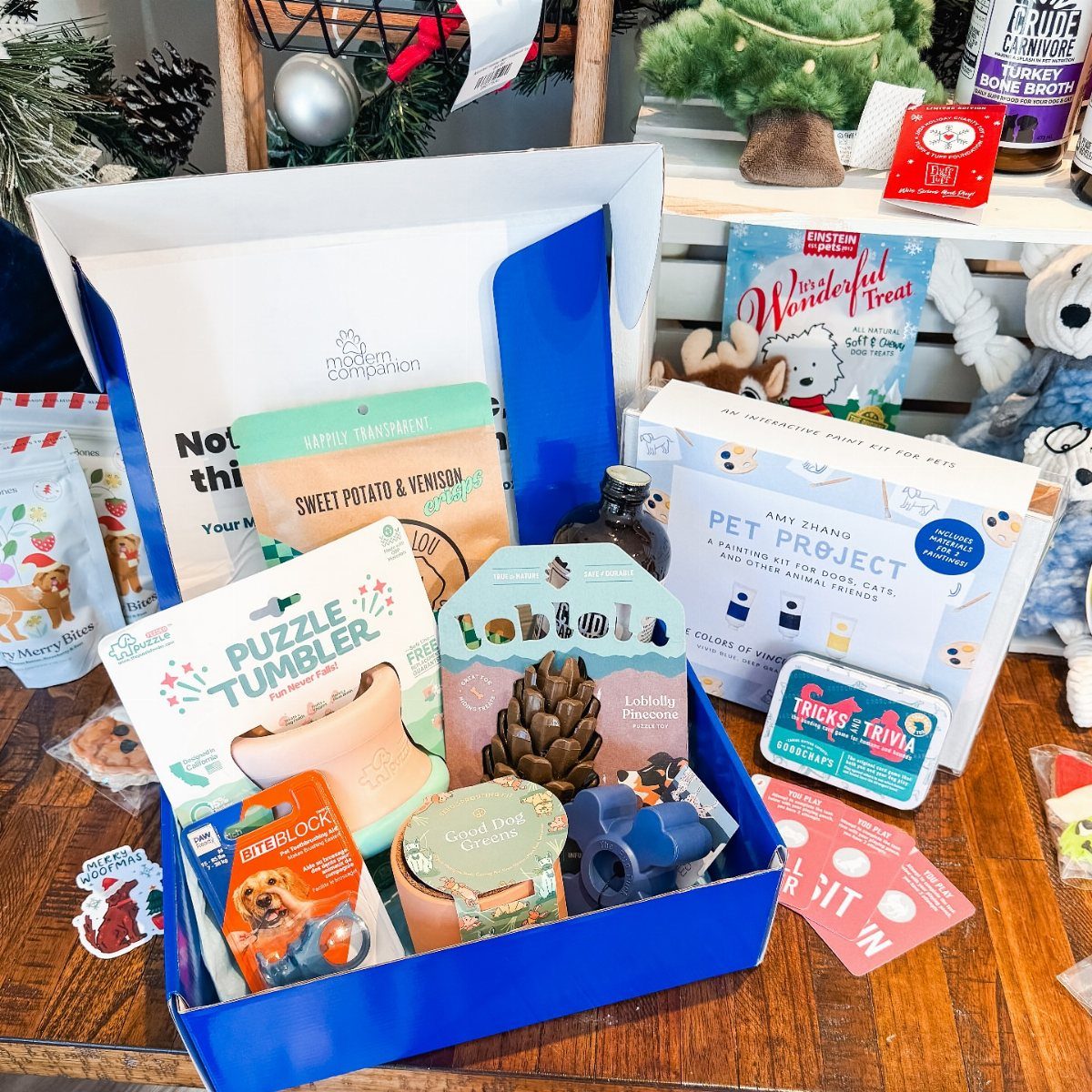 Blue gift box filled with dog toys and treats on a wooden table.