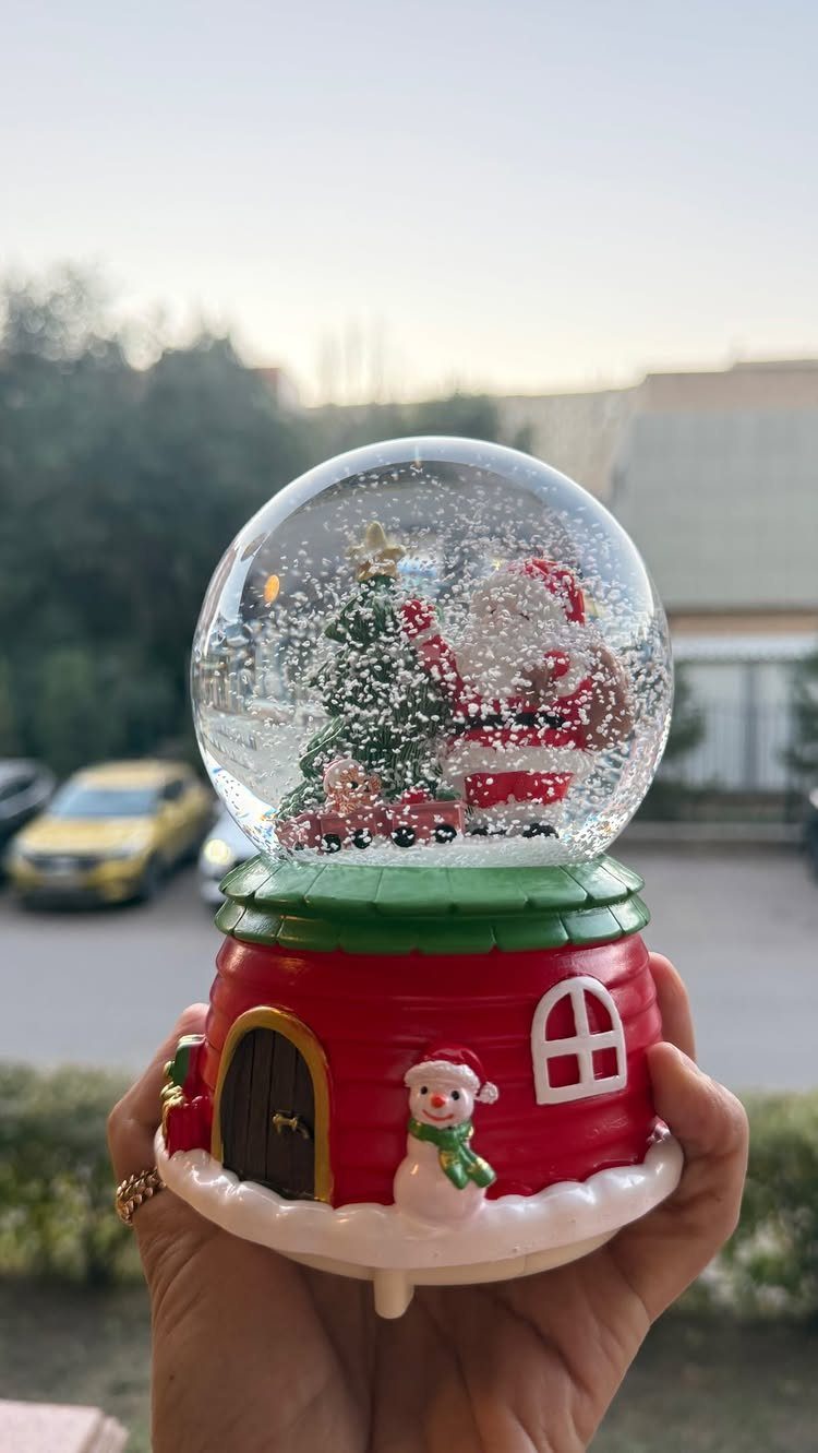 Christmas snow globe with Santa and a snowman held in a hand.