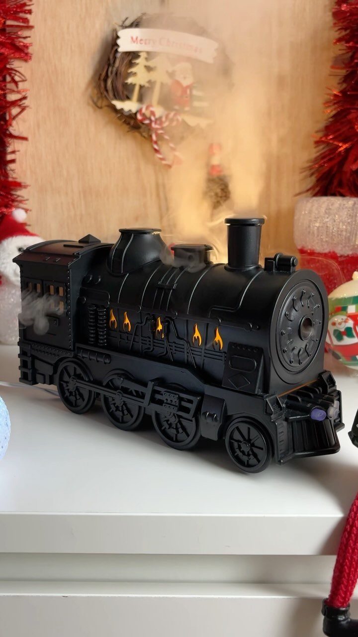 Black toy steam locomotive with orange lights on a white surface with holiday decorations