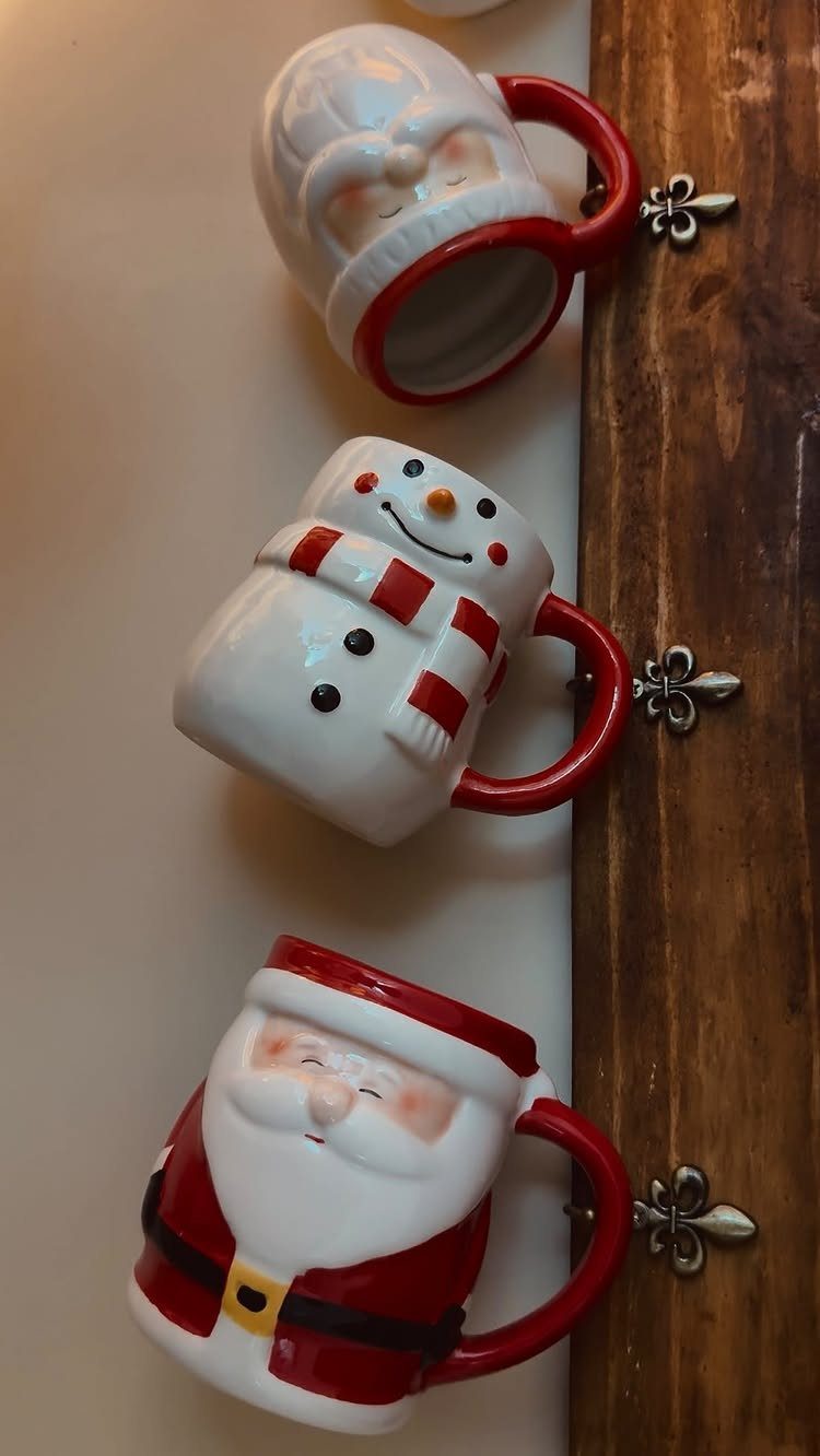 Three festive ceramic mugs shaped like Santa and a snowman on a wooden rack