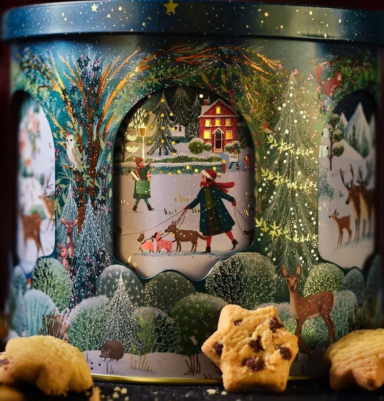 Festive blue holiday tin with a lit window scene and star-shaped cookies.