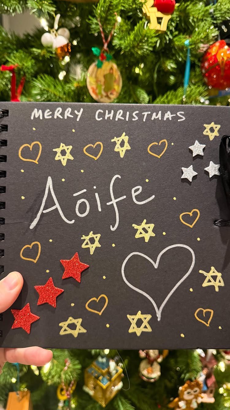 Handmade black Christmas notebook with white lettering and gold star decorations held up.