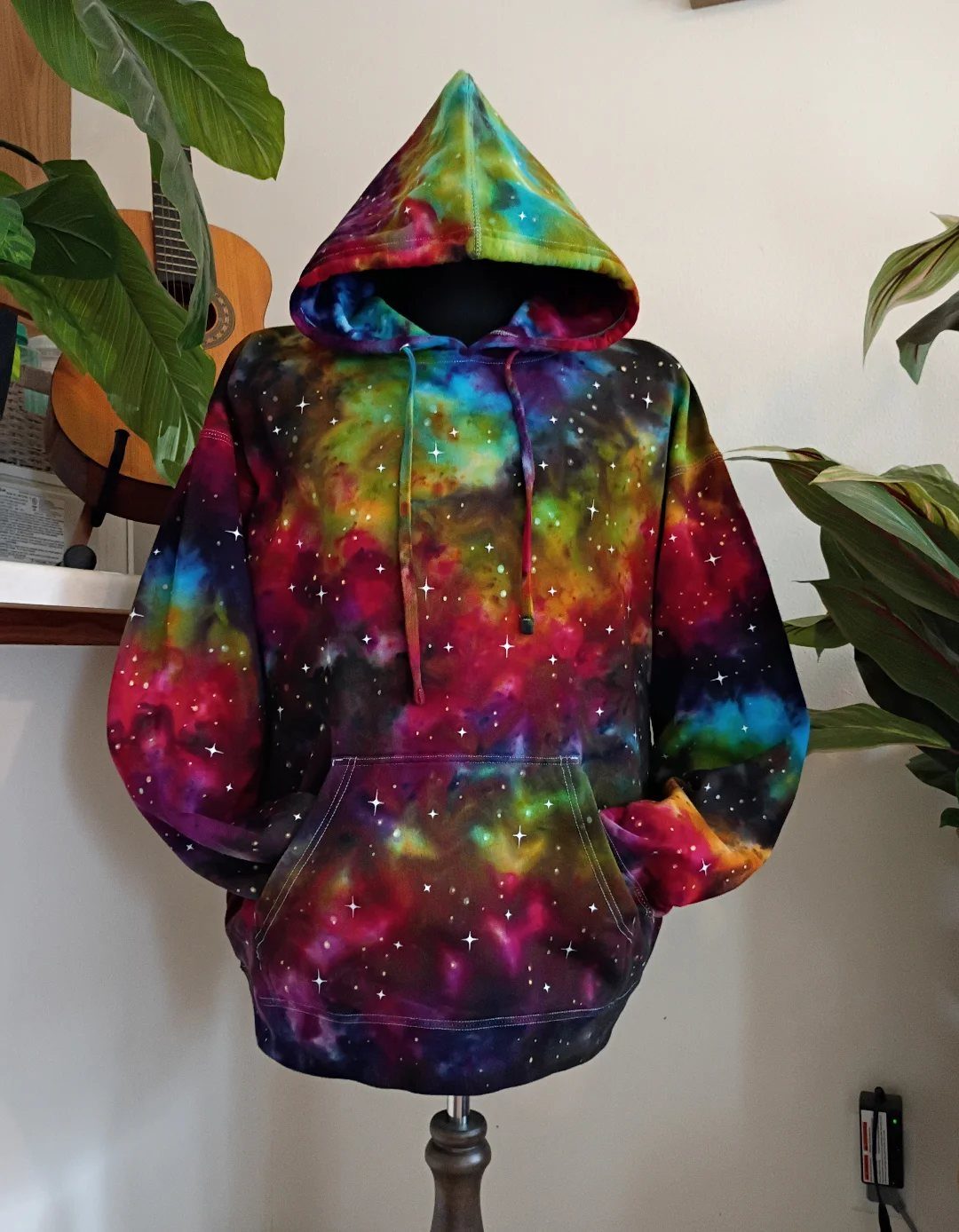 Galaxy print hoodie with colorful nebula patterns displayed on a mannequin indoors.