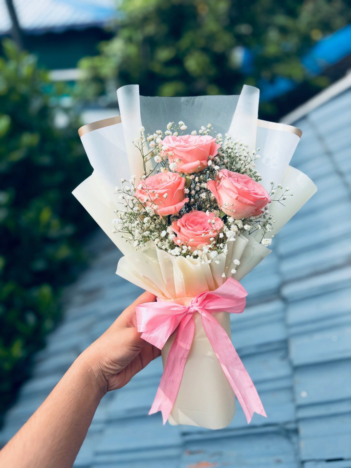 Small bouquet of pink roses and baby's breath wrapped in white paper.