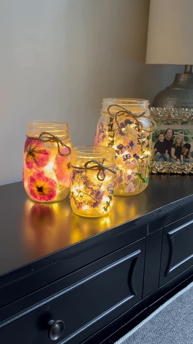 Three mason jars filled with pressed flowers and fairy lights on a dresser.