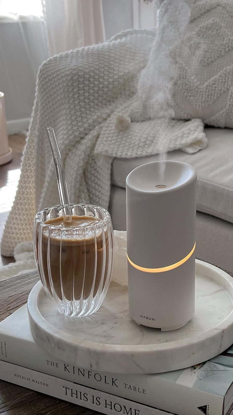 White essential oil diffuser emitting steam next to iced coffee on marble tray