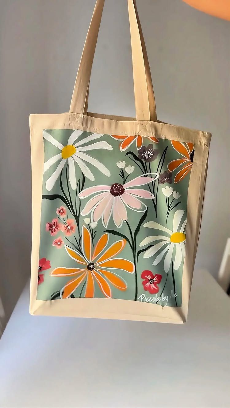 Beige canvas tote bag with a colorful floral daisy print on a green background.
