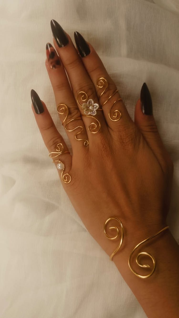 Hand wearing gold wire-wrapped spiral rings and a matching cuff bracelet.