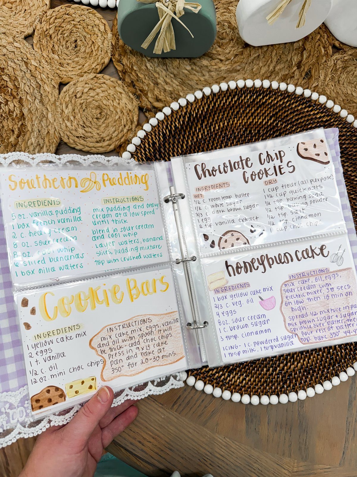 Handwritten recipe cards in a white binder resting on a woven brown tray.
