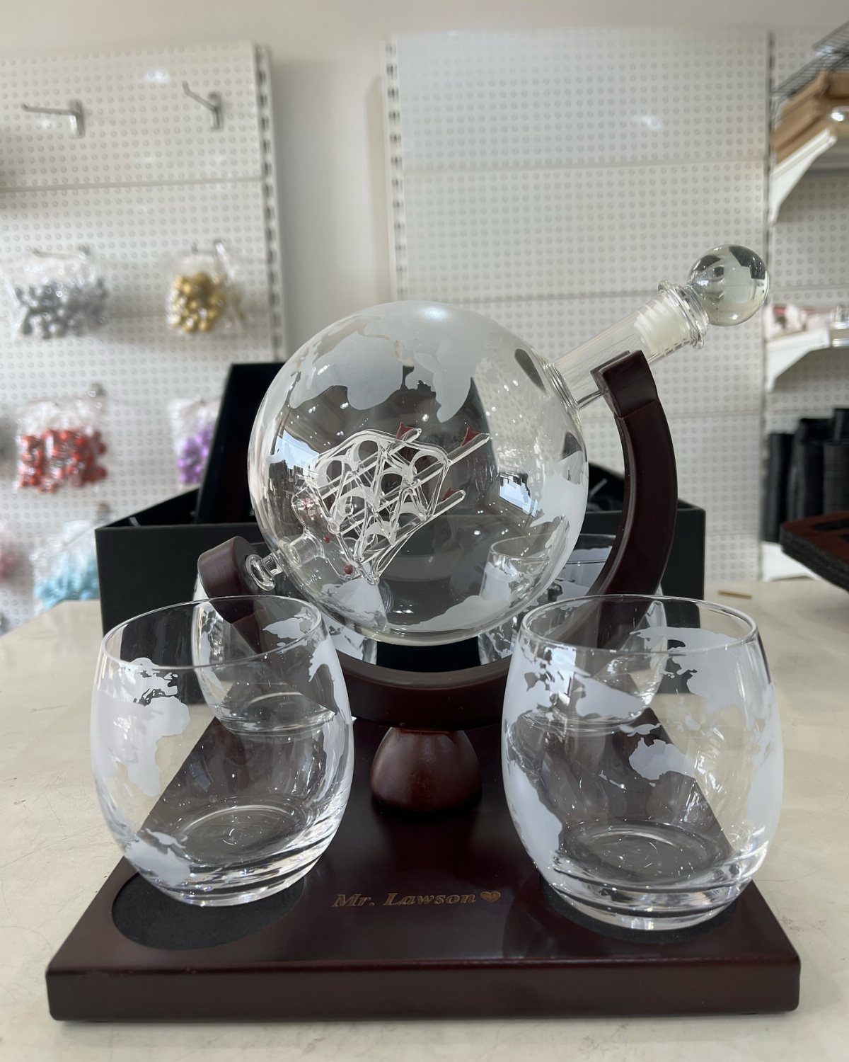 Globe-shaped glass wine decanter and two matching glasses on a wooden engraved stand.