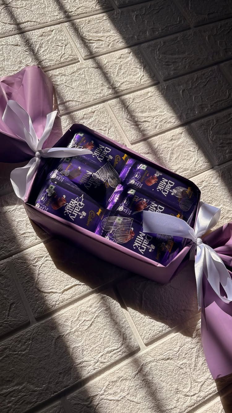 Purple gift box filled with chocolate bars tied with white ribbons on white bricks.