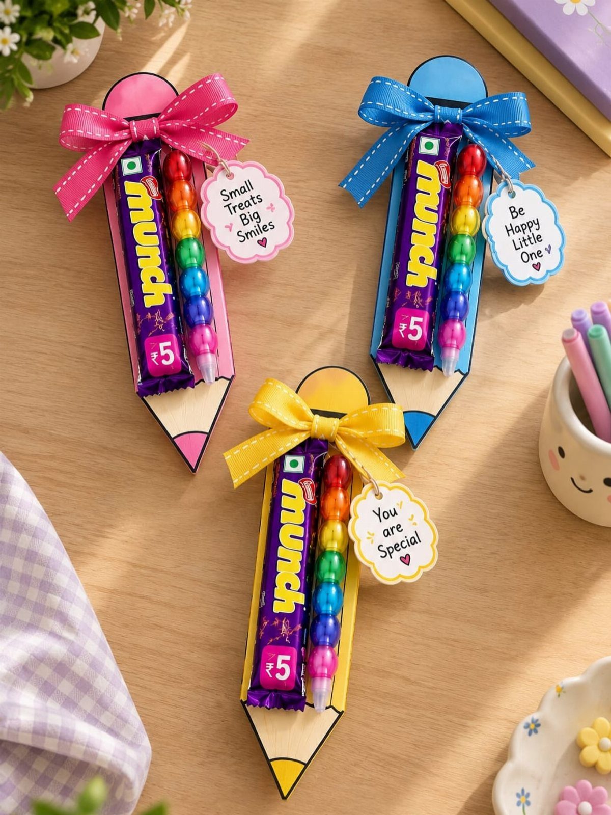 Pencil-shaped gift holders with chocolate bars, crayons, and handwritten notes on wood.
