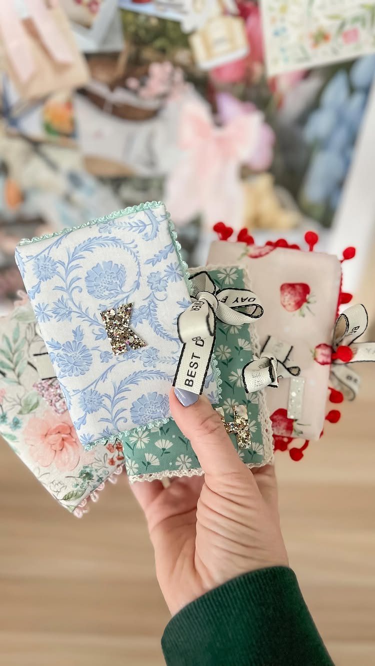 Handmade floral fabric pouches with ribbons and pom-poms held in a person's hand.