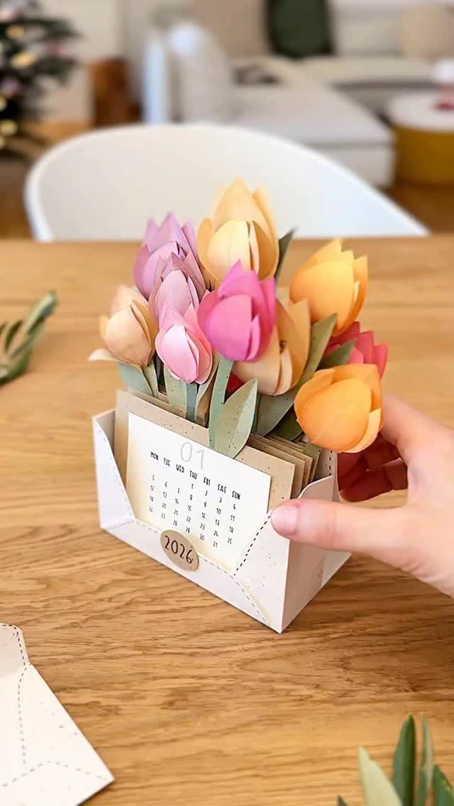 Hand holding a small paper gift box with colorful paper tulips and a calendar.