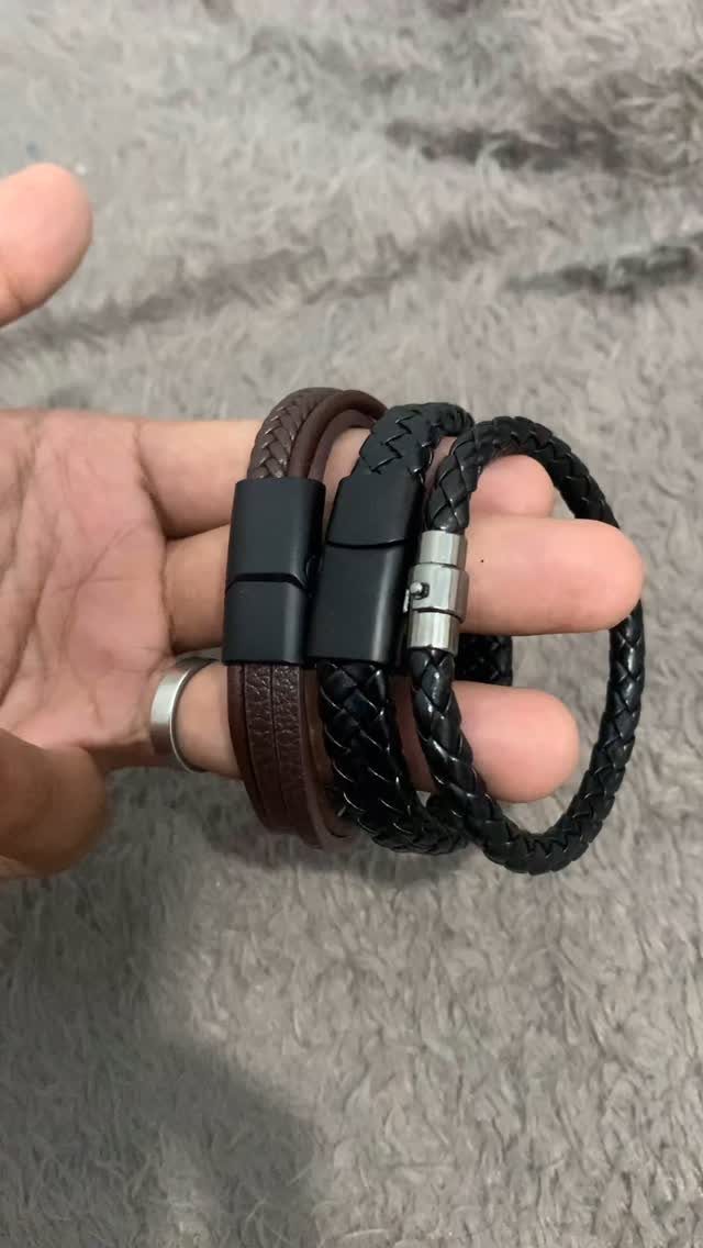 Three braided leather bracelets in brown and black held in a hand.
